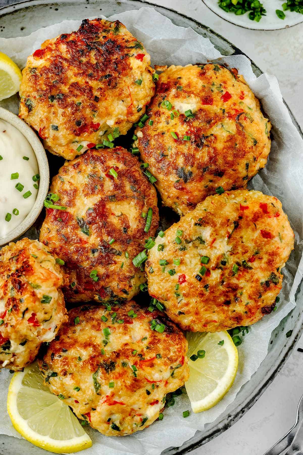 Savory shrimp cakes arranged on a plate, garnished with lemon slices and served with zesty lime-chili mayo.