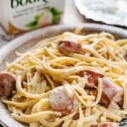 Boursin Cheese Pasta with Smoked Sausage served on a plate, a pack of Boursin Cheese in the background.
