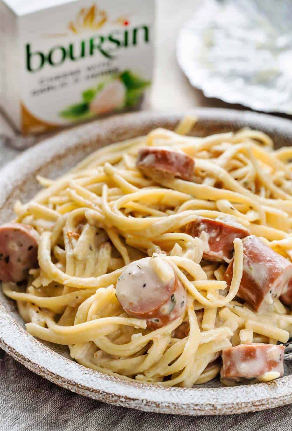 Boursin Cheese Pasta with Smoked Sausage served on a plate, a pack of Boursin Cheese in the background.