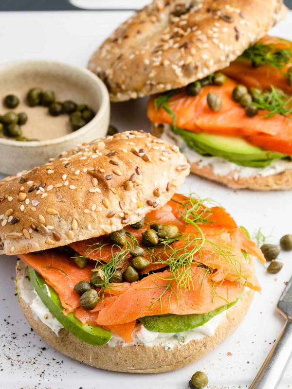 Two smoked salmon bagels on a serving board, garnished with fresh dill and capers.