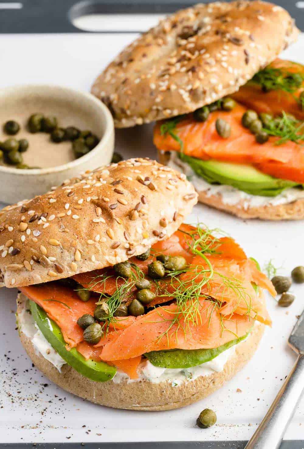 Two smoked salmon bagels on a serving board, garnished with fresh dill and capers.