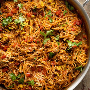 Steaming skillet of homemade taco spaghetti with ground beef, melted cheese, and spaghetti noodles, garnished with fresh cilantro.