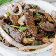 Savory beef and onion stir fry served on a plate, garnished with green onions .
