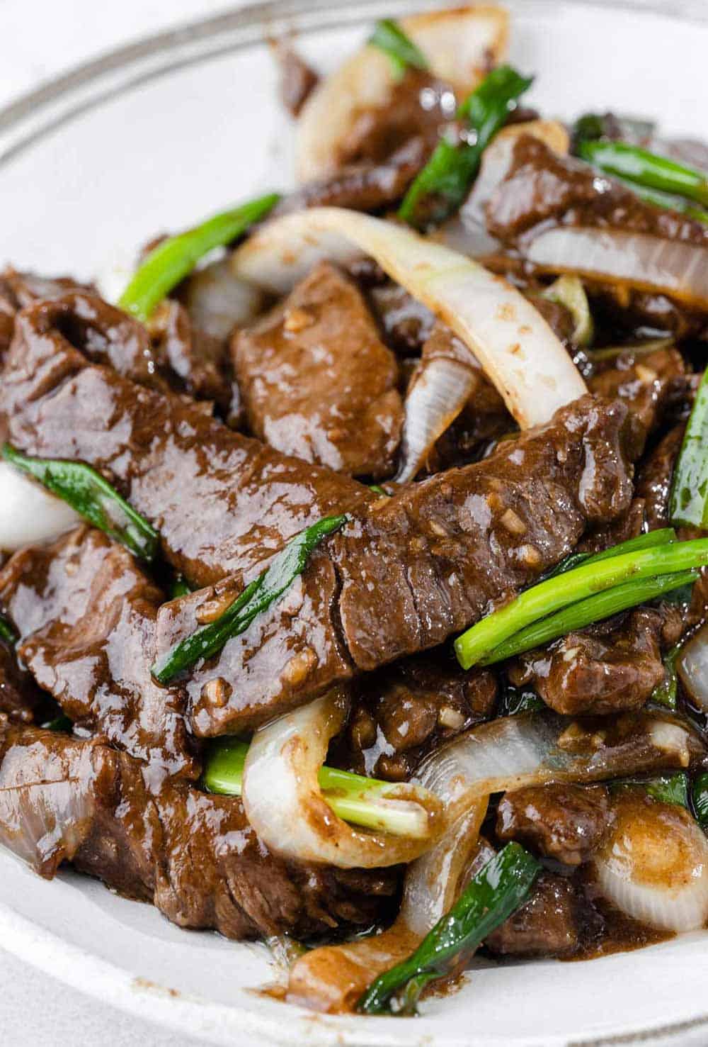 Savory beef and onion stir fry served on a plate, garnished with green onions .