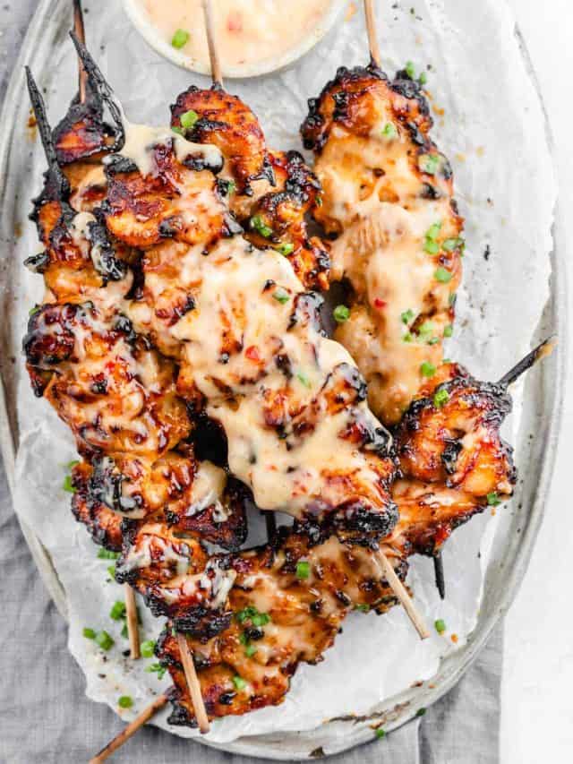 Plate of succulent Bang Bang Chicken Skewers with creamy sauce and garnished with green onions.