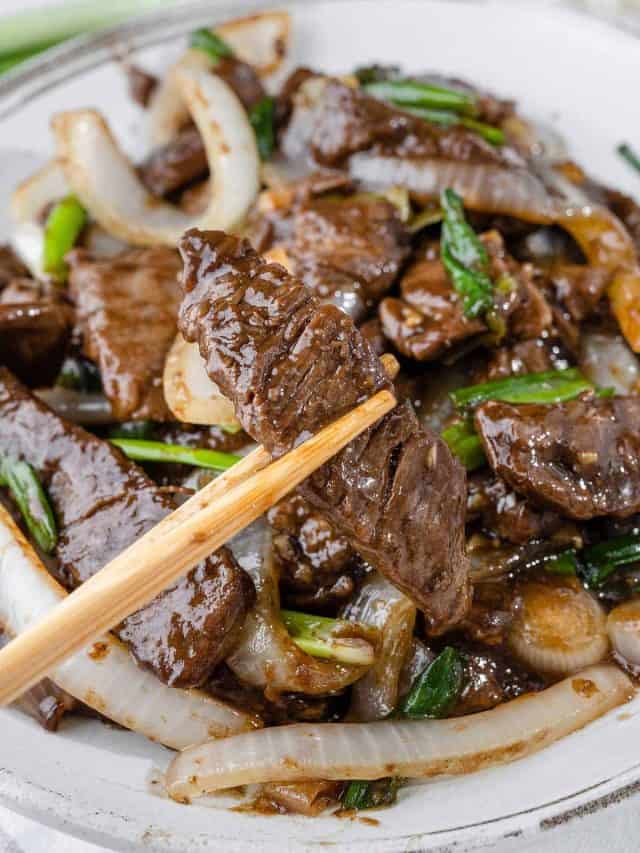 Holding a tender strip of beef with chopsticks, showcasing its juicy texture.