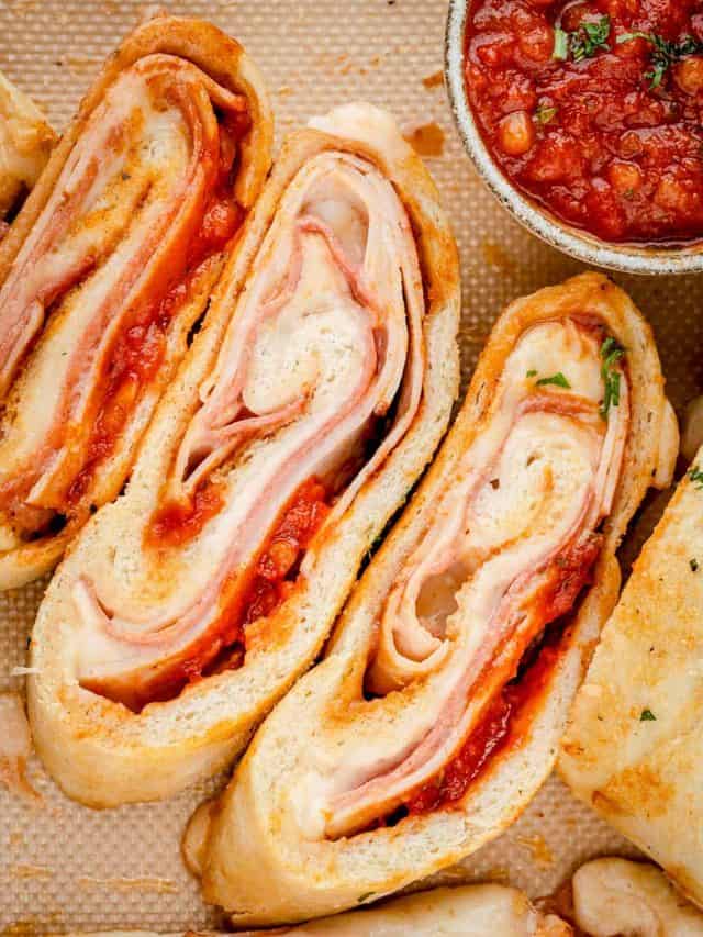 Overhead view of sliced stromboli on a silicone mat, displaying its golden crust and layered fillings inside.
