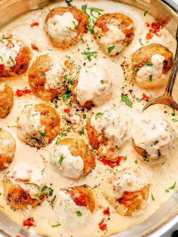 Golden-brown turkey pesto meatballs served in a creamy sun-dried tomato Alfredo sauce in a skillet.
