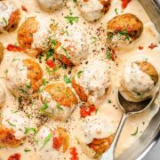 Close-up top view of turkey pesto meatballs in a creamy sun-dried tomato Alfredo sauce, in a skillet with a serving spoon.