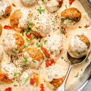 Close-up top view of turkey pesto meatballs in a creamy sun-dried tomato Alfredo sauce, in a skillet with a serving spoon.