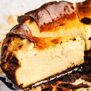 Holding a slice of San Sebastian Cheesecake on a spatula, displaying its creamy texture and caramelized edges.