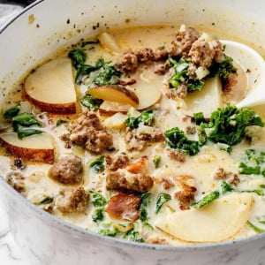 Image of Zuppa Toscana Soup in a Dutch oven. The soup is creamy and abundant with Italian sausage, potato slices, and kale, showcasing a variety of colors and textures.