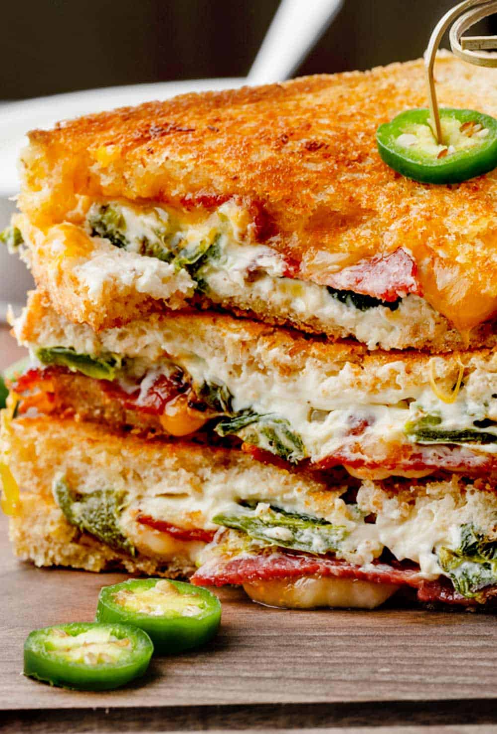Image of a jalapeno popper grilled cheese sandwich cut diagonally and placed on a wooden serving board. The sandwich reveals melted cheese, bacon and roasted jalapeno pieces inside.