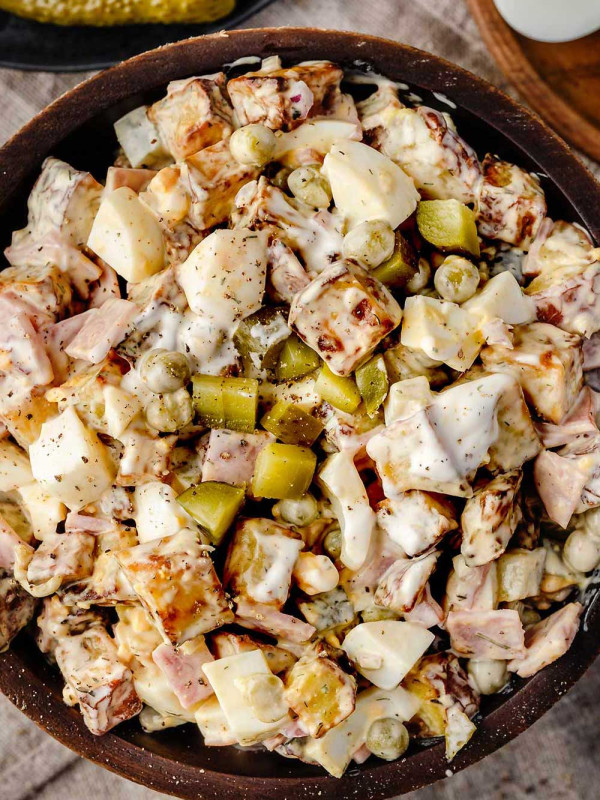Dill Pickle Potato Salad in a wooden bowl, featuring creamy potatoes, crunchy dill pickles, deli ham, peas and a zesty dressing.