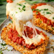 Crispy baked chicken fillets being generously topped with warm marinara sauce and melted mozzarella cheese.