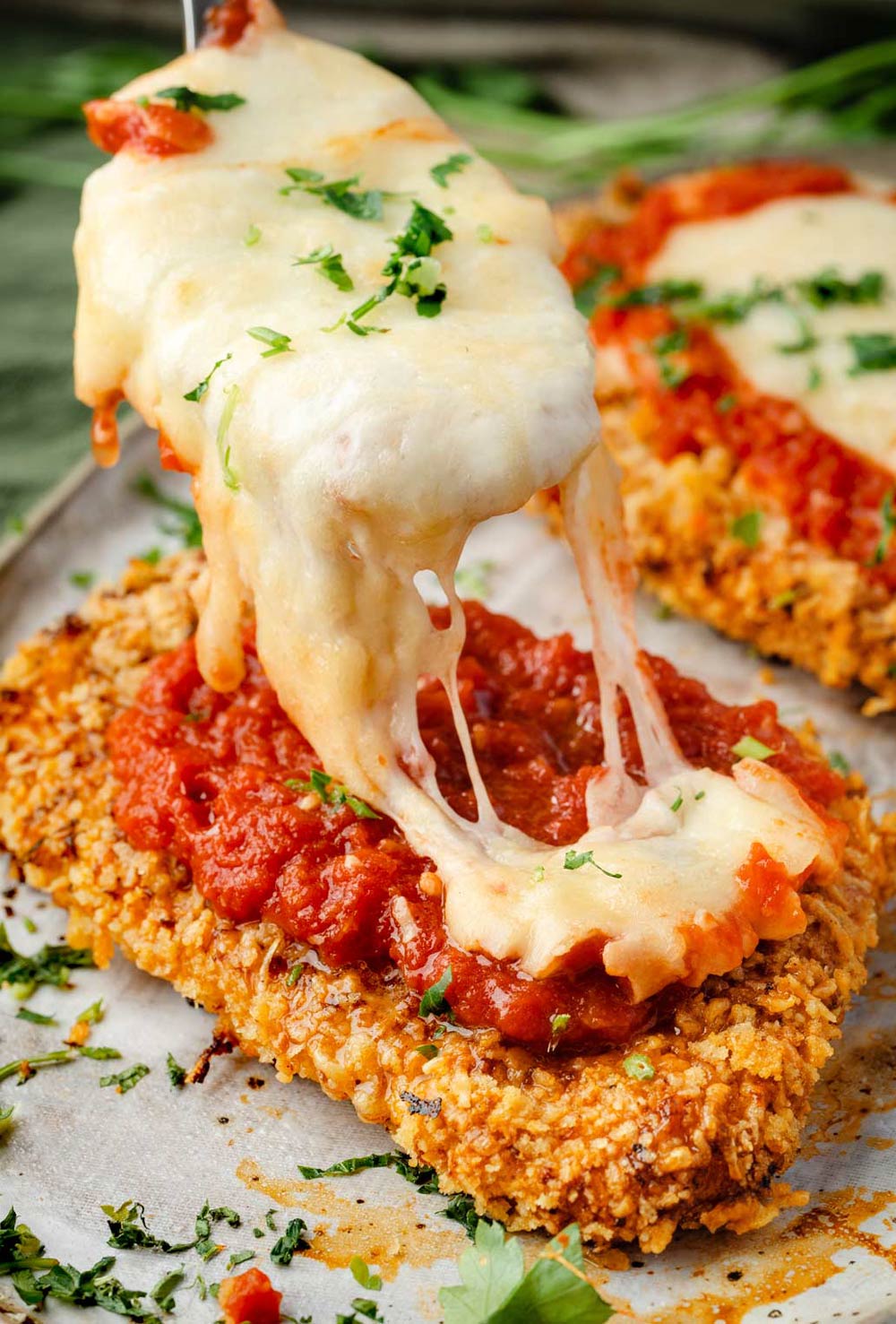 Crispy baked chicken fillets being generously topped with warm marinara sauce and melted mozzarella cheese.