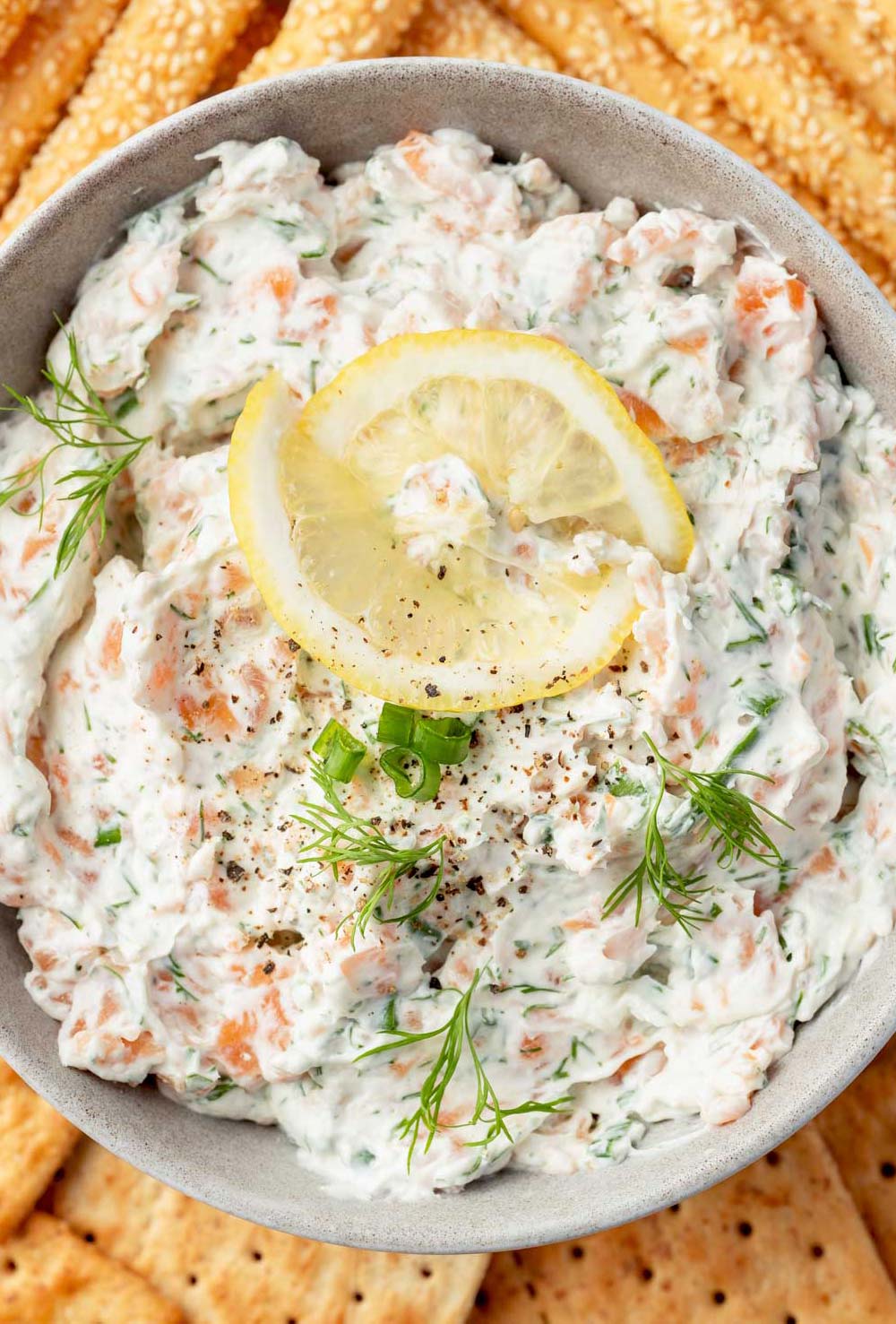 The overhead image of bowl filled with creamy smoked salmon dip, garnished with thinly sliced lemon rounds and sprigs of fresh dill.