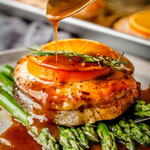 A close-up image shows a round salmon steak on a white plate, with a vibrant orange glaze being poured over it.