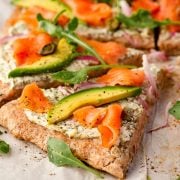Close-up of a Smoked Salmon Pizza slice with smoked salmon, red onion, capers, avocado, and arugula.