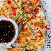 Overhead image of Korean pancakes cut into bite-sized pieces, arranged on a plate, and served with a small bowl of dipping sauce on the side.
