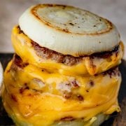 Close-up image of the Onion-Wrapped Flying Dutchman, featuring two golden brown beef patties encased in caramelized onion rings, with melted cheese.