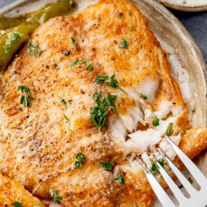 Close-up of a tilapia fillet being flaked with a fork, revealing its tender and juicy interior.