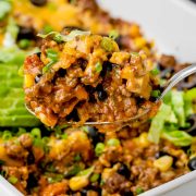 Close-up of a spoon filled with taco casserole, showcasing layers of ground beef, cheddar cheese, salsa, and crunchy Doritos, held above the casserole dish.