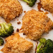 Overhead shot of crispy Oven Fried Chicken Thighs and roasted broccoli, with a small bowl of honey garlic sauce nestled on the tray.