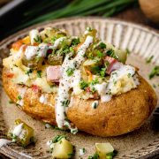 A close-up of a Dill Pickle and Ham Twice Baked Potato on a plate, drizzled with creamy sour cream.