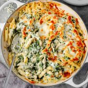 Overhead view of a cheesy spinach dip chicken pasta casserole, with golden, bubbly cheese on top.