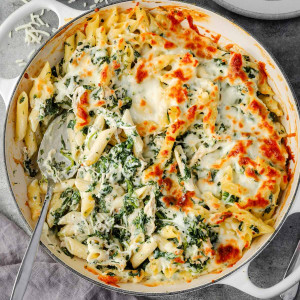 Overhead view of a cheesy spinach dip chicken pasta casserole, with golden, bubbly cheese on top.