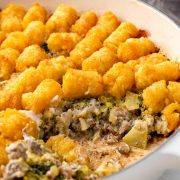 A close-up image of Tater Tot Casserole, featuring golden, crispy tater tots on top of a hearty layer of ground beef, broccoli, melted cheese, and creamy sauce.