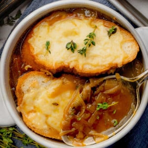 A bowl of Longhorn French onion soup topped with toasted baguette slices covered in melted cheese, with a spoon resting in the soup.