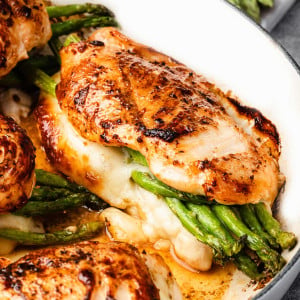 Close-up of Asparagus Stuffed Chicken Breast in a skillet, showing juicy golden-brown chicken, melted cheese, and vibrant green asparagus spears.