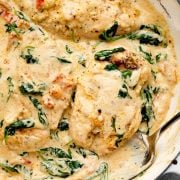 Creamy baked Tuscan chicken in a rich garlic parmesan sauce, featuring tender chicken breasts, wilted spinach, and sun-dried tomatoes, served in a skillet with a spoon.