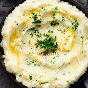 Overhead view of a bowl filled with creamy garlic mashed potatoes, topped with fresh chives and parsley.