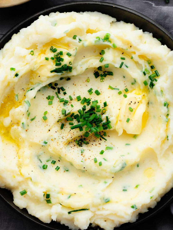 Overhead view of a bowl filled with creamy garlic mashed potatoes, topped with fresh chives and parsley.