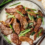 Overhead image of a bowl containing P.F. Chang's style Mongolian beef, featuring thinly sliced beef glazed in a savory sauce, garnished with green onions.
