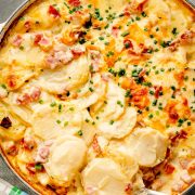 Creamy Ranch Scalloped Potatoes and Ham topped with melted cheese and fresh chives, served in a casserole dish.