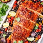 The image shows baked blackened salmon with roasted veggies, black beans, lime wedges, and a side of mango avocado salsa.