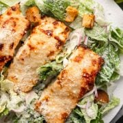 A close-up of Parmesan Crusted Salmon Caesar Salad with crispy salmon, fresh romaine lettuce, creamy dressing, crunchy croutons, and grated Parmesan cheese on top.