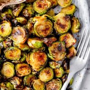 A plate of roasted Brussels sprouts drizzled with balsamic glaze, served with a fork.