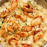 Golden, seared chicken strips sit on a bed of creamy garlic Parmesan rice, garnished with fresh parsley in a stainless steel skillet.