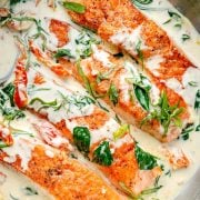 Seared salmon fillets in a creamy Tuscan sauce with spinach, sun-dried tomatoes, and fresh basil in a skillet.