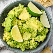 A bowl of chunky guacamole with fresh lime wedges, served with crispy tortilla chips.