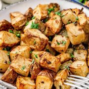 A plate of golden, crispy roasted potatoes garnished with fresh parsley, with a Lipton onion soup mix box and dipping sauce in the background.