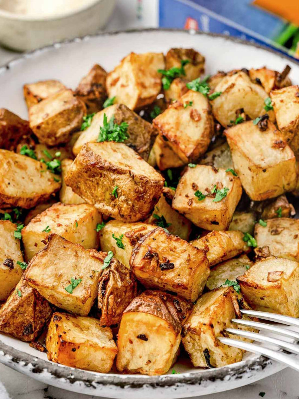 A plate of golden, crispy roasted potatoes garnished with fresh parsley, with a Lipton onion soup mix box and dipping sauce in the background.