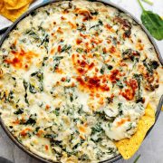 Creamy baked spinach and artichoke dip topped with golden melted cheese, served in a skillet with tortilla chips on the side.