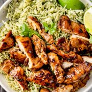 A bowl of juicy, pan-seared Chipotle-style chicken served over vibrant cilantro lime rice with fresh lime wedges.