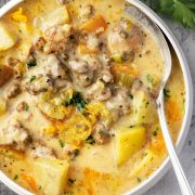 A bowl of creamy potato and hamburger soup with chunks of potatoes, ground beef, and melted cheese, garnished with fresh parsley.